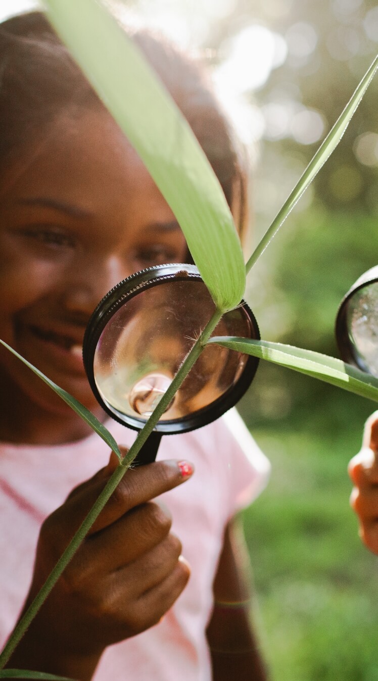 Young girl looking at a plant with a magnifying glass in Sunbridge community, St. Cloud, Florida in Metro Orlando