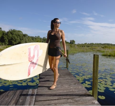 A woman carrying stand-up paddleboard while walking along a dock in Sunbridge community, St. Cloud, Florida in Metro Orlando