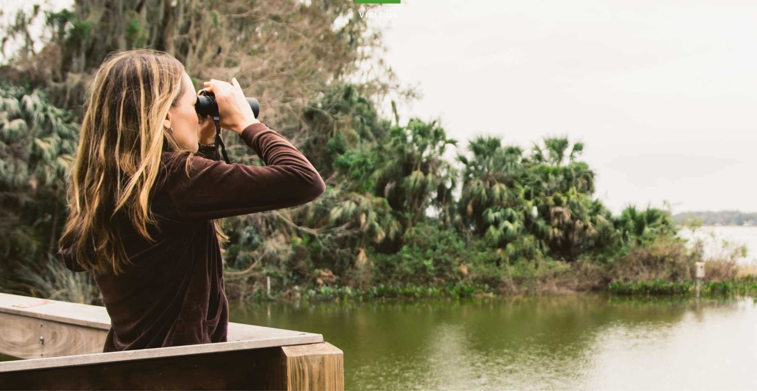 Woman using binoculars to look out over a lake while standing on a pier in Sunbridge community, St. Cloud, Florida in Metro Orlando